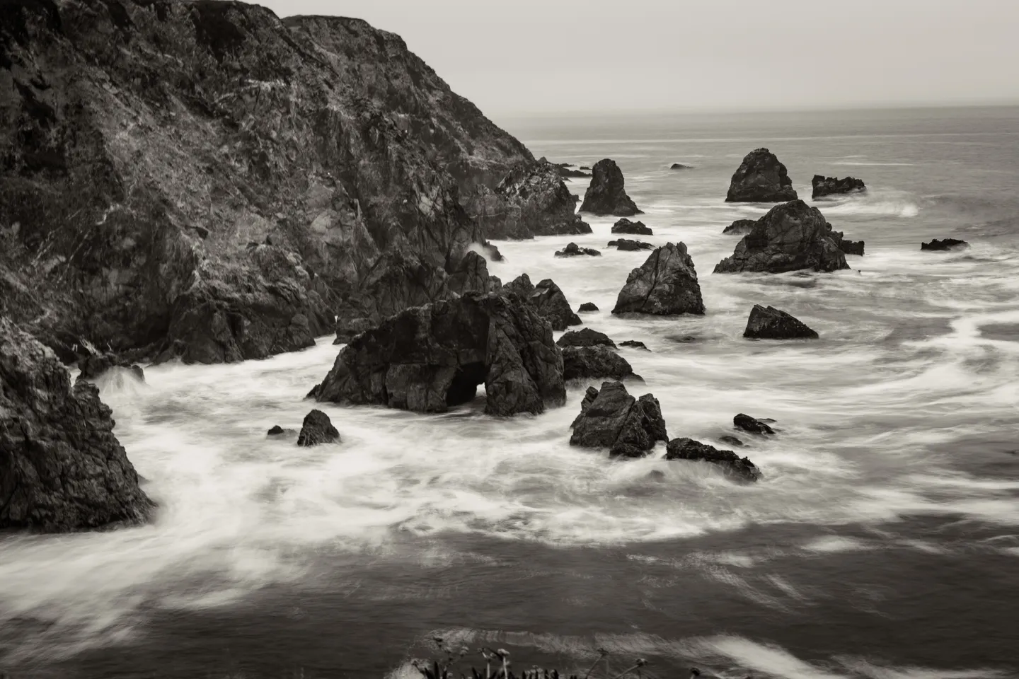 Black-and-white photograph of ocean waves along a rocky coastline